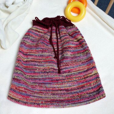 Mehrfarbiger gestrickter Babyschlafsack mit dunkelroter Kordel auf hellem Tuch