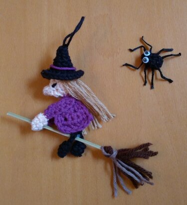 Gehäkelte kleine Hexe mit Besen und eine kleine Spinne vor orangefarbenem Hintergrund