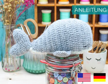 Gehäkelter grauer Amigurumi-Wal mit gesticktem Auge auf Glasdose mit Knöpfen