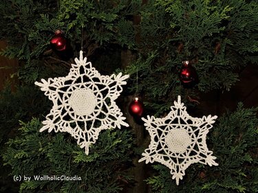 Zwei weiße sternförmige Häkelapplikationen als Dekoration an Nadelbaumzweigen