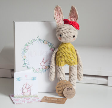 Gehäkeltes Amigurumi-Häschen mit gelbem Körper, roter Schleife und Geschenkbox