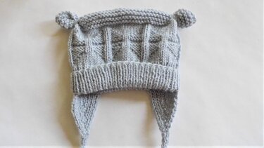 Hellgraue gestrickte Babymütze mit Ohrenklappen und zwei kleinen Öhrchen auf hellem Hintergrund