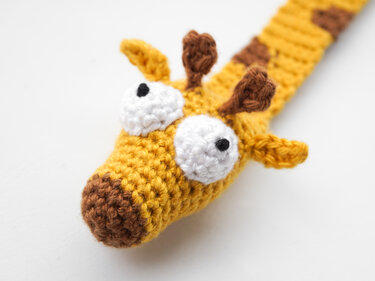 Crocheted giraffe bookmark head with yellow yarn, brown snout, small horns, and white eyes