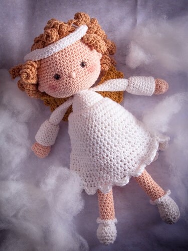 Gehäkelte Amigurumi-Engelspuppe mit Locken, weißem Kleid, Flügeln und Stirnband auf watteartigen Wolken