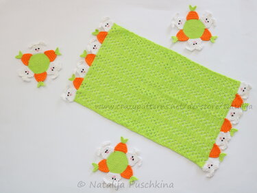 Frühlingsgrüner Häkel-Läufer mit aufgesetzten weißen Hasen und orangen Karotten, ergänzt durch runde Hasen-Untersetzer