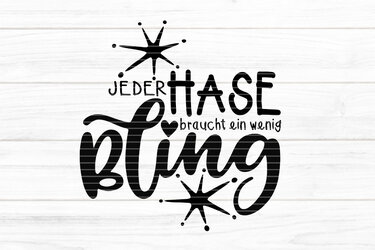 Schwarzer Schriftzug „Jeder Hase braucht ein wenig Bling“ mit stilisierten Sternen und Herz auf hellem Holzbrett‑Hintergrund.