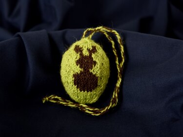 Gestrickte hellgrüne Eiform mit braunem Hasenmotiv und Aufhängekordel auf dunkelblauem Stoff