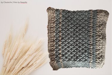 Gestrickter Kissenbezug in Grau und Beige mit Rautenmuster neben Getreideähren