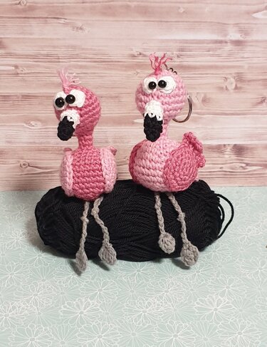 Zwei rosa gehäkelte Flamingos, einer mit Schlüsselring, auf schwarzem Garn.
