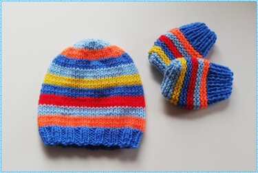 Gestrickte Babymütze und ein Paar Schühchen mit bunten horizontalen Streifen auf hellem Hintergrund.