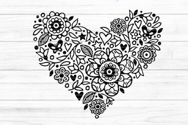 Schwarz-weißes Herz aus filigranen Blumen, Blättern und Schmetterlingen auf hellem Holzuntergrund.