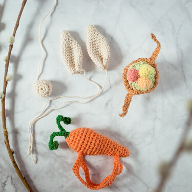 Schnell gehäkelte Oster-Accessoires: Hasenohren, Karottenform, Nest mit bunten Pompoms und kleine Kugel