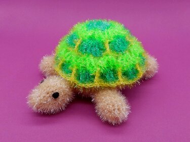 Gehäkelte flauschige Schildkröte mit grün-gelbem Panzer auf rosa Hintergrund