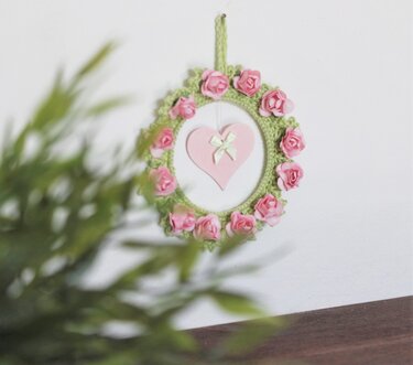 Runde Hängedekoration mit grüner Häkelumrandung, rosa Rosen und hängendem rosa Herz