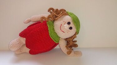Gehäkelte Amigurumi-Puppe mit rotem Kleid, grünem Kragen, grüner Mütze und braunen Locken