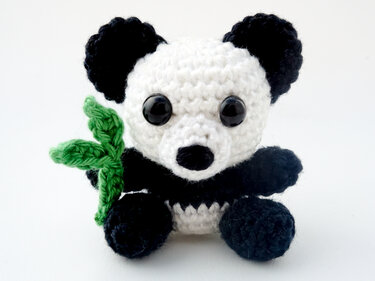 Black-and-white crocheted panda amigurumi holding a small green bamboo leaf on a white background.