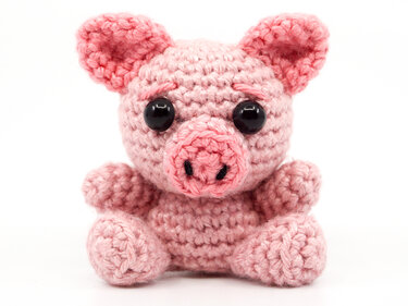Small pink crocheted amigurumi pig with round black eyes on a white background