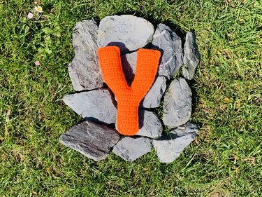 Orangefarbener gehäkelter Buchstabe Y auf grauen Steinen im Gras