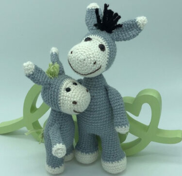 Zwei gehäkelte Esel-Amigurumi in Grau und Weiß, ein großer und ein kleiner, vor hellem Hintergrund.