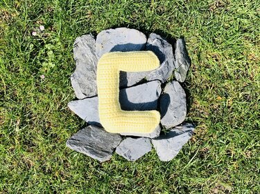 Gehäkelter gelber Buchstabe C auf grauen Steinen im Gras