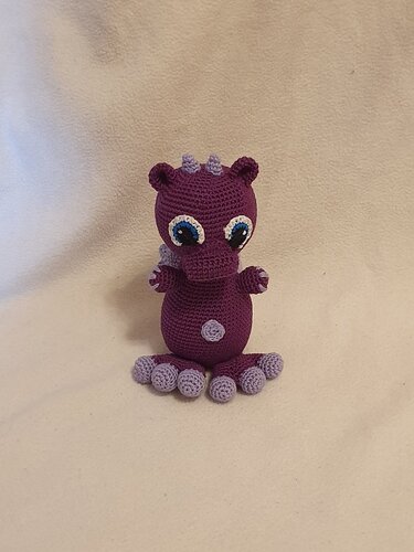 Gehäkelter lila Amigurumi-Drache mit blauen Augen und hellvioletten Akzenten