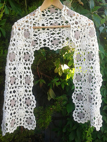 White lacy crochet scarf with floral motifs hanging on a wooden hanger against green foliage