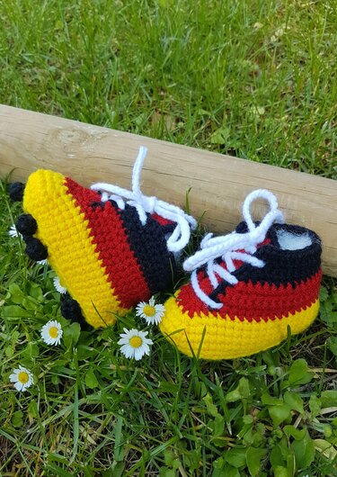 Gehäkelte Babyschnürer in Schwarz, Rot und Gelb mit weißen Schnürsenkeln auf Gras