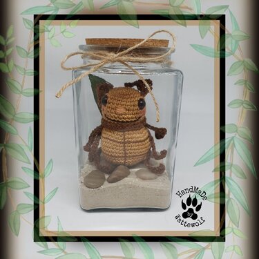 Kleines gehäkeltes Käfer-Amigurumi dekorativ in einem Glas mit Sand, Kieseln und Korkband