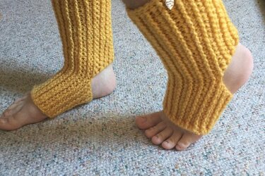 Gelbe gehäkelte Beinstulpen mit Fußschlaufe an nackten Füßen auf Teppich