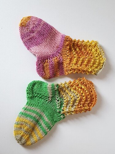 Zwei gestrickte Babysocken, eine pink-lila mit gelb-orangefarbenem Schaft, eine grün mit gestreifter Spitze