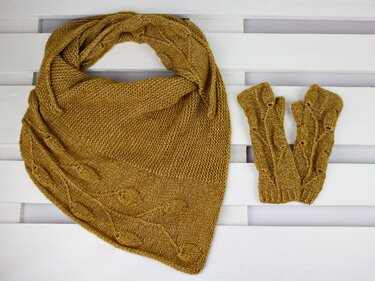 Gestricktes senfgelbes Dreieckstuch und fingerlose Handschuhe mit Blättermuster auf weißem Holzuntergrund.