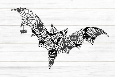 Schwarze Fledermaus-Silhouette aus Halloween-Symbolen auf hellem Holzuntergrund.