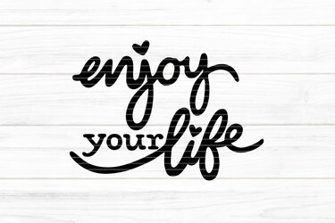 Schwarzer Script‑Schriftzug „enjoy your life“ mit Herz‑Details auf hellem Holzuntergrund