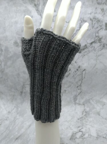 Dunkelgraue gestrickte fingerlose Armstulpe mit Daumenloch auf weißer Modellhand, Rippenstruktur