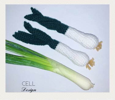 Zwei gehäkelte Frühlingszwiebeln in Weiß und Dunkelgrün, daneben eine echte Frühlingszwiebel zum Vergleich.