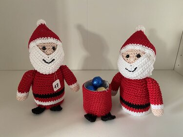 Gehäkelter Weihnachtsmann mit Zahlenanhänger 17 neben einem roten Häkelsäckchen mit Schokokugeln sowie einer zweiten Weihnachtsmann-Figur.