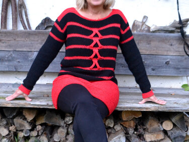 Damen-Strickpullover schwarz-rot mit mittigem Kreuzdetail, sitzend auf Holzbank