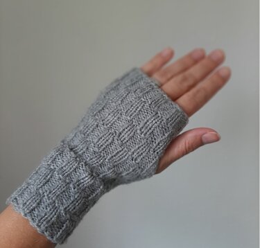 Hand wearing a light grey knitted fingerless glove with textured stitch pattern and ribbed cuff
