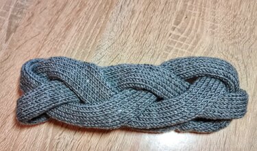 graues gestricktes Stirnband mit Zopfmuster auf Holzuntergrund