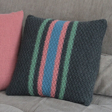 Gestricktes anthrazitfarbenes Kissen mit vertikalen Streifen in Hellblau, Rosa und Mintgrün auf einem Sofa