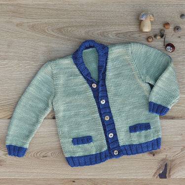 Mintgrüne Kinderstrickjacke mit blauen Details und hellen Holzknöpfen auf Holzuntergrund.