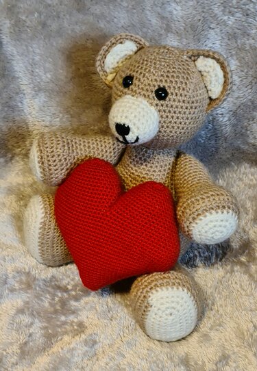 Gehäkelter Teddybär im Amigurumi-Stil mit rotem Herz vor grauem Hintergrund
