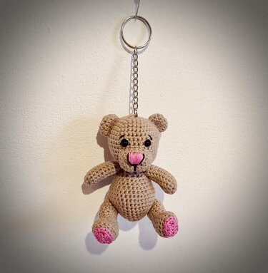 Hellbrauner gehäkelter Amigurumi-Teddybär als Schlüsselanhänger mit Metallkette, rosa Nase und rosa Pfoten an einem silbernen Schlüsselring