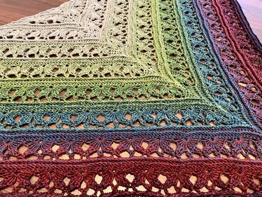 Gehäkeltes Dreieckstuch, Detailaufnahme mit Farbverlauf von Creme über Grün bis Blau und Rot sowie offenem Spitzenmuster