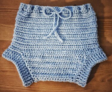 Hellblaue gehäkelte Baby-Windelhose flach auf Holzuntergrund mit Kordel