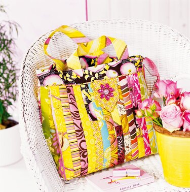 Bunte Streifen-Patchwork-Tasche in Gelb und Pink auf weißem Korbstuhl mit Blumenapplikation