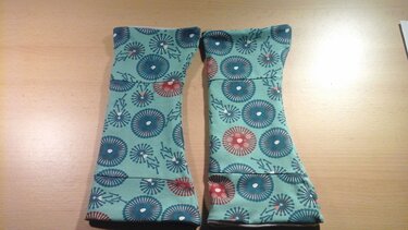 Ein Paar fertig genähter Stulpen aus mintgrünem Stoff mit blau-rotem Kreismuster liegt nebeneinander auf einem Holztisch.