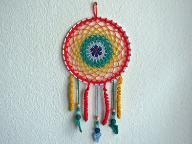 Bunter gehäkelter runder Wandbehang mit konzentrischem Muster, Holzperlen und hängenden Quasten an weißer Wand