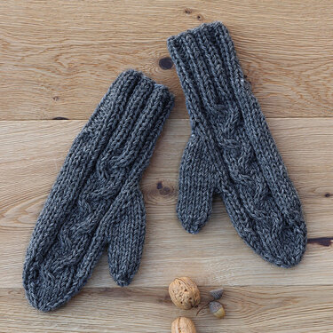 Graue gestrickte Damen-Fäustlinge mit Zopfmuster auf hellem Holz