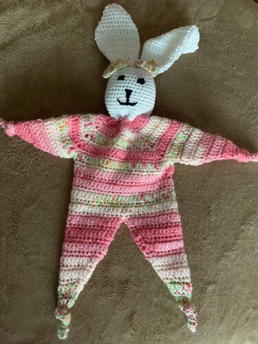 Gehäkeltes Häschen‑Schmusetuch in Rosa und Pastell mit langen Ohren und geknoteten Zipfeln auf braunem Untergrund